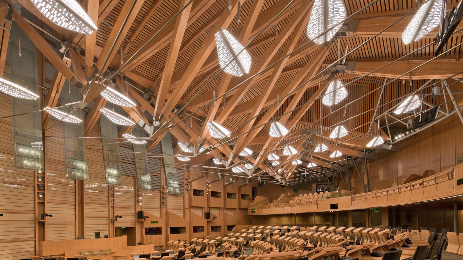 A large wooden conference hall, a wooden structure in the ceiling with a lighting design resembling floating leaves