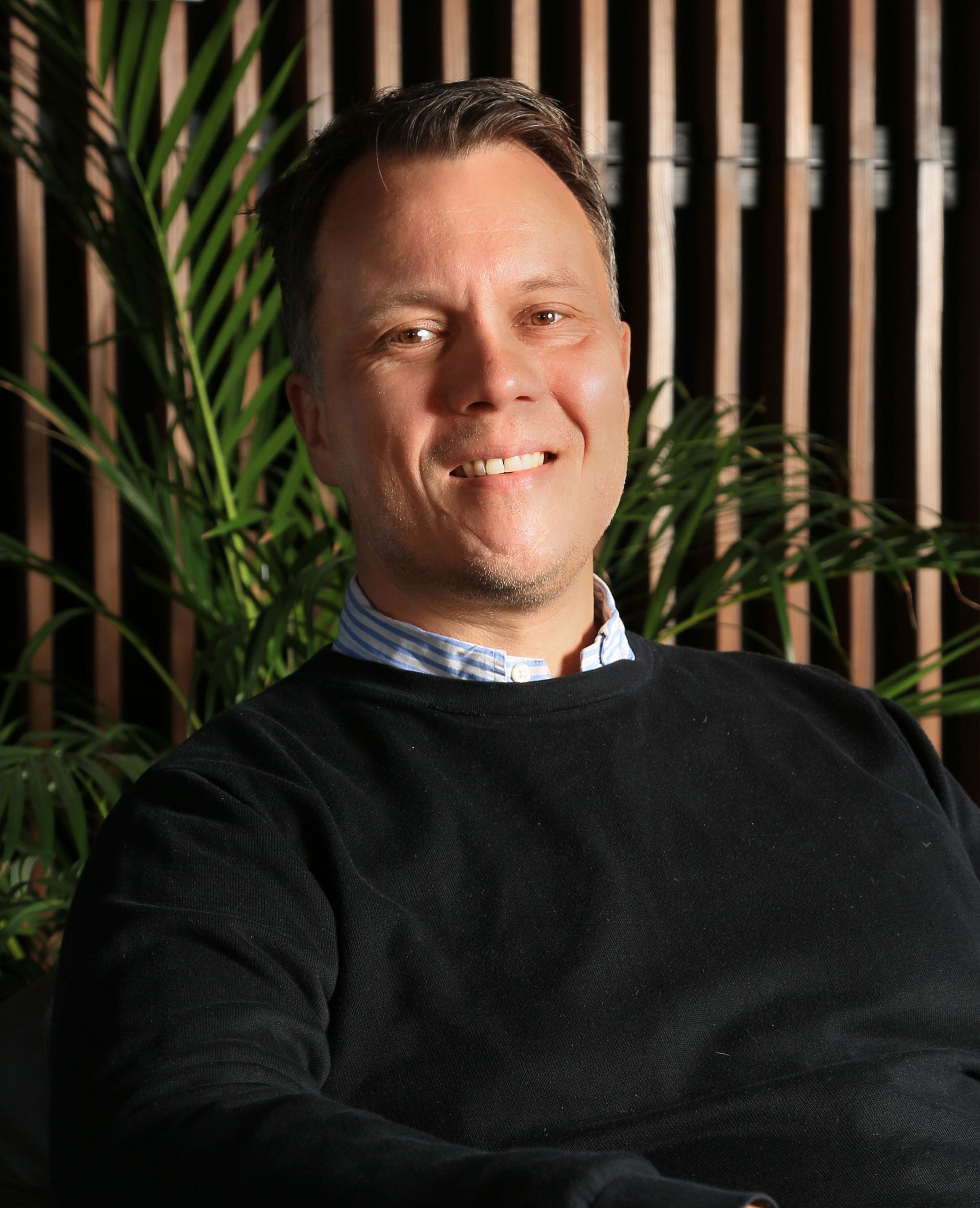 Portrait of a man, green plants and wooden panel in background