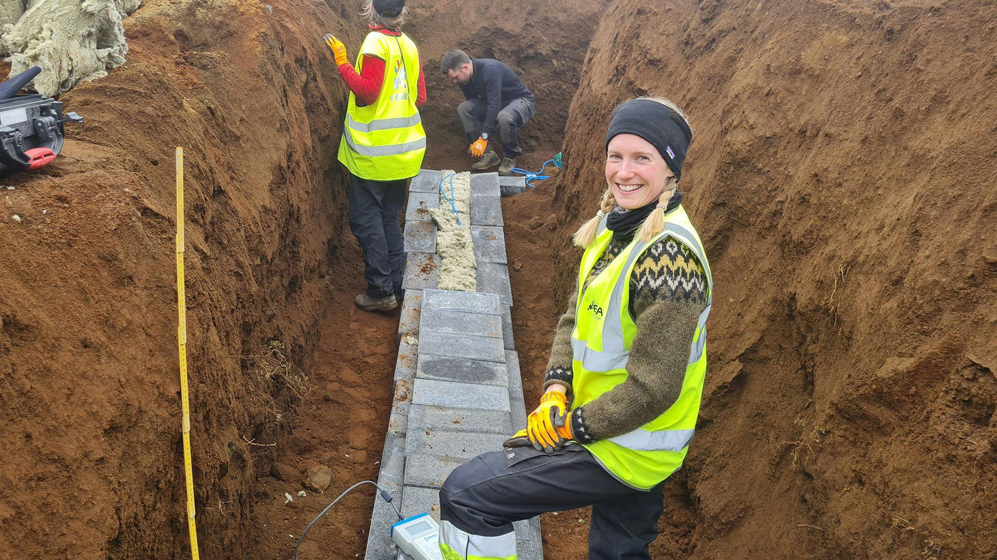 A woman with a smile, accompanied by another woman and a man at a dug-up site