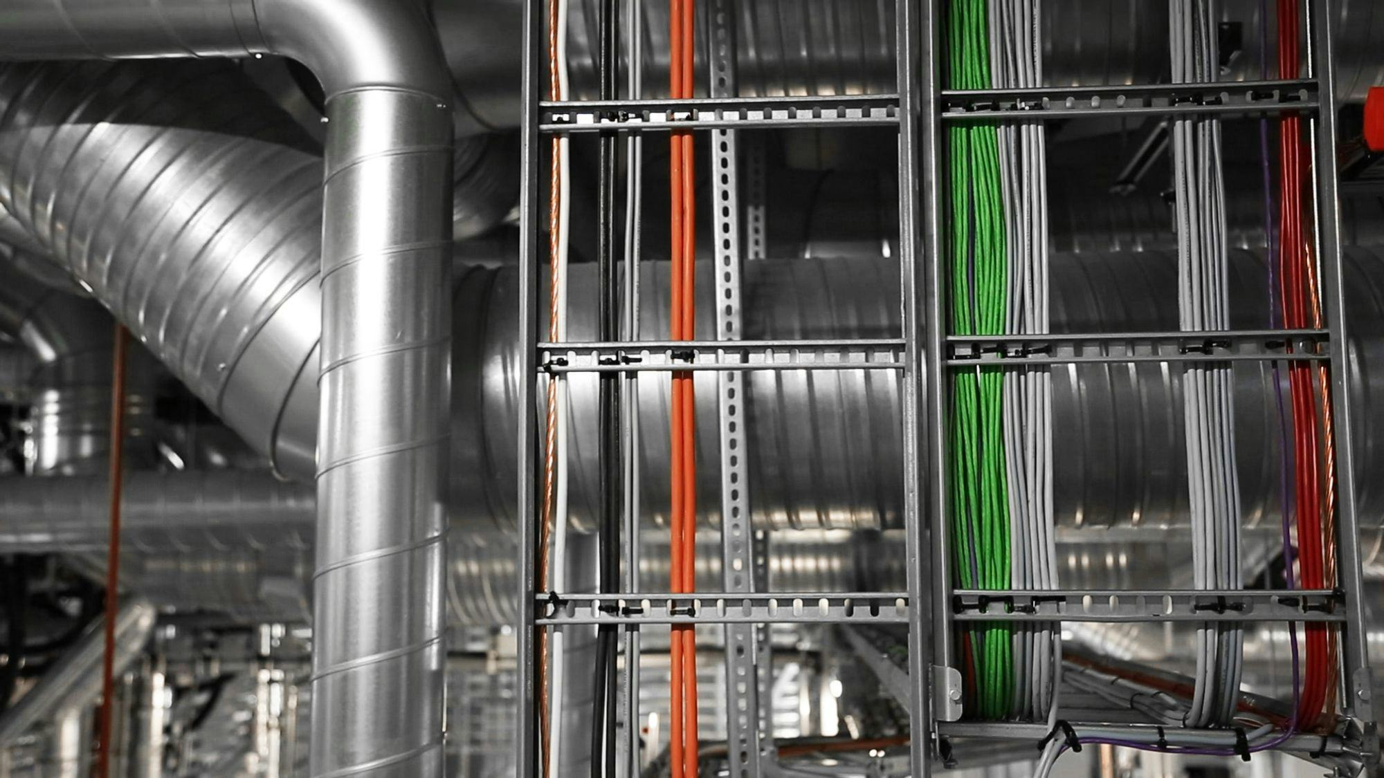Ventilation system in the background and electrical cables in orange, green, green and red colors on a frame in the foreground