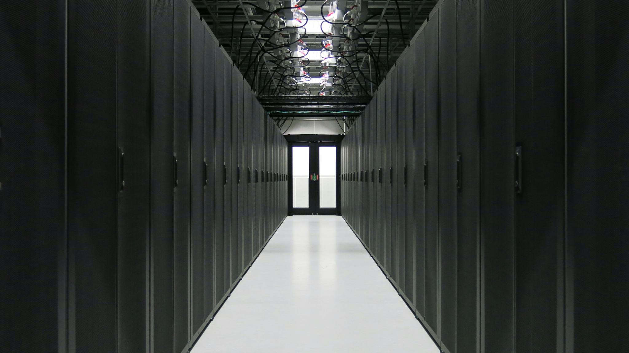 A long corridor with black cupboards on both sides, a front door at the end of the corridor. Cables from the black cabinets connected to a wire structure in the ceiling