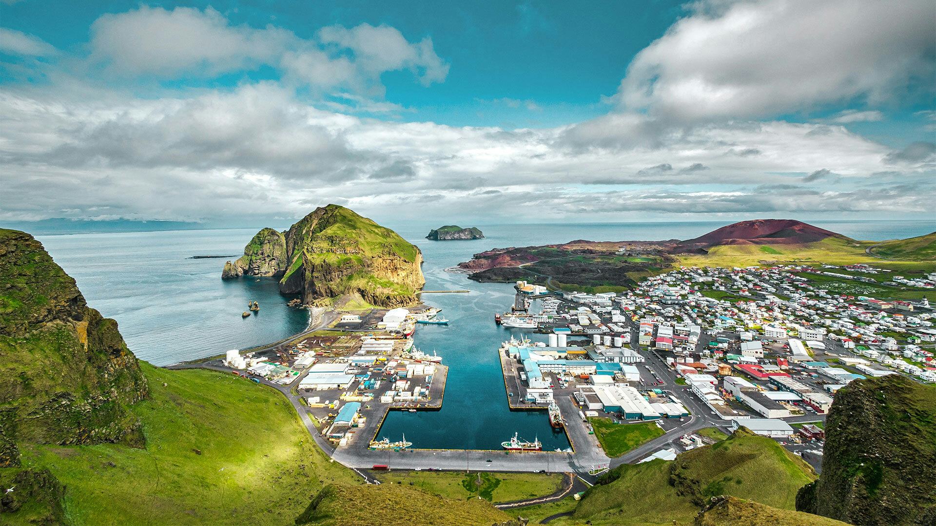 Aerial view of the Vestmanna Islands, seen from land and out to sea. A small town by the sea, mountains and grasslands