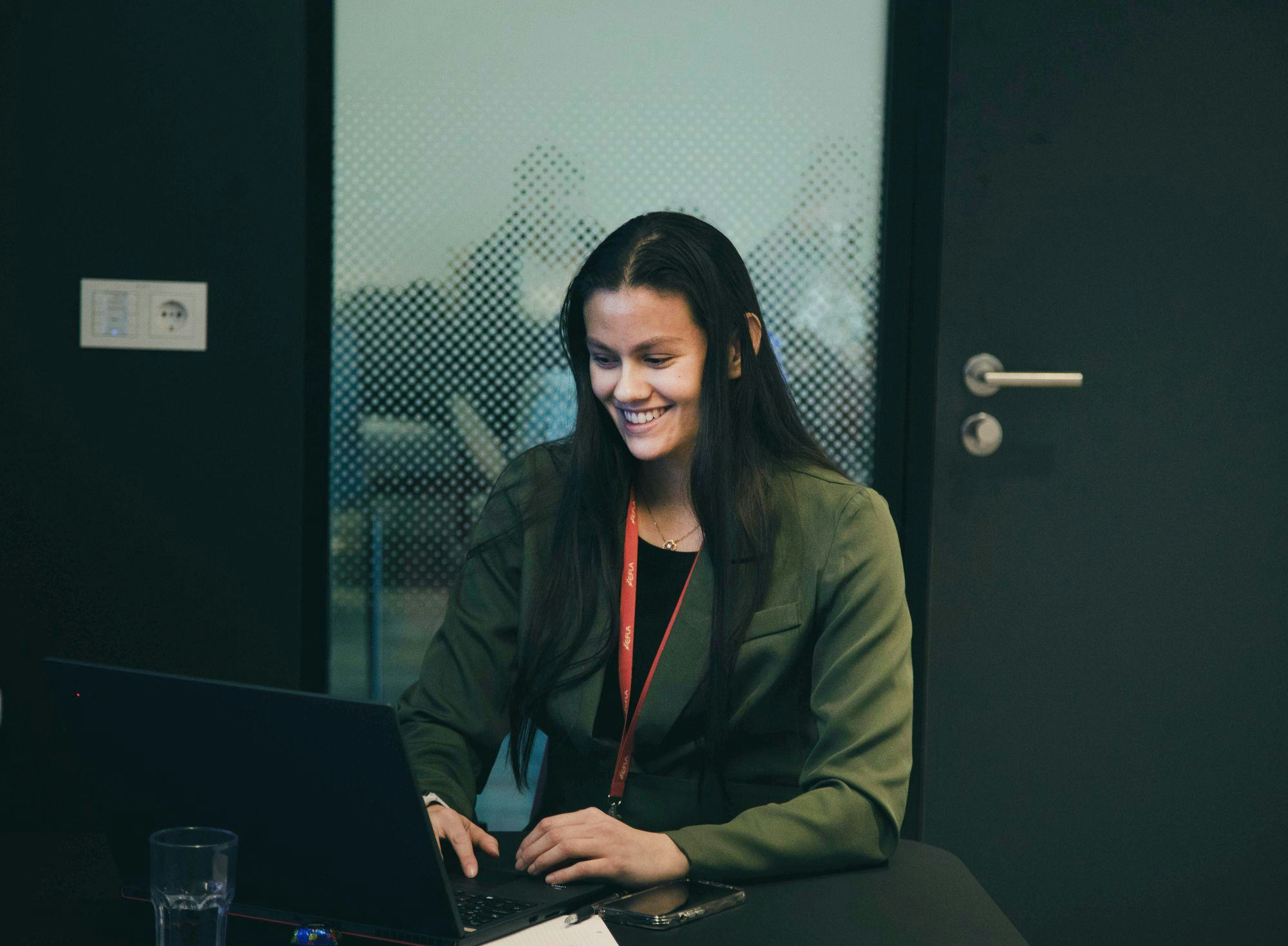 A young woman working on a laptop smiling and looking at the screen