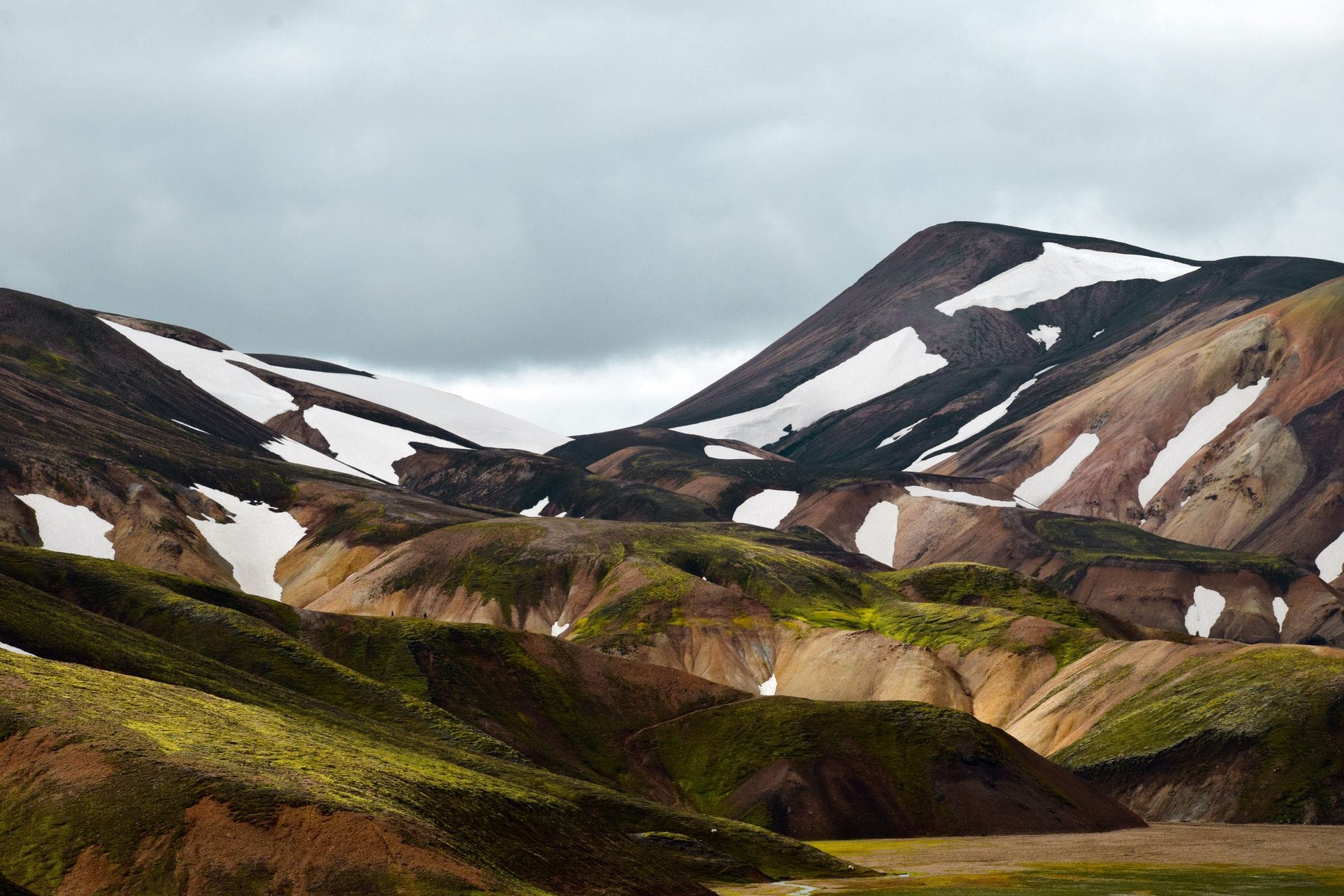 Sun and shadows fall on mountainous terrain with occasional snow patches on the highest peaks